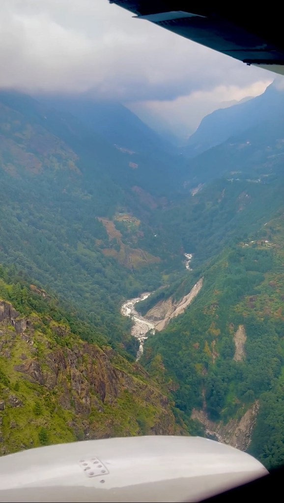 Aerial view of green mountains and river valley from small aircraft window on flight from Manthali to Lukla Nepal