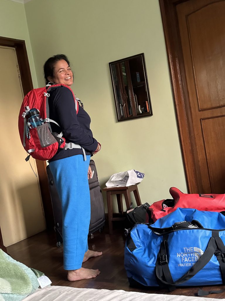 Woman with red backpack and travel bags smiling while packing for Everest Base Camp trek in Nepal